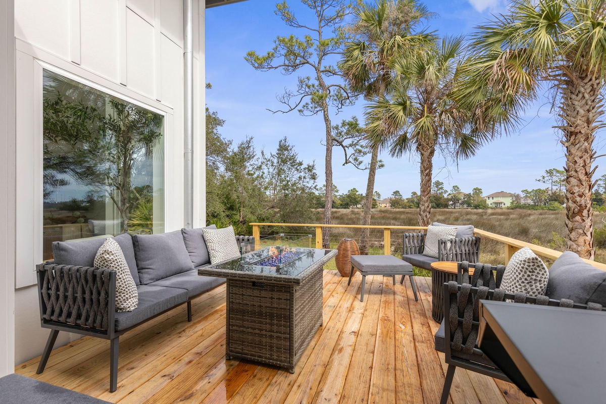 Deck with a fire table and lounge seating overlooking the marsh and palm trees