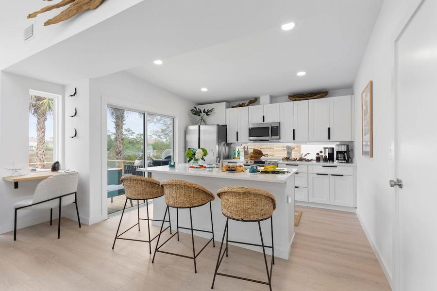 White kitchen with an island, woven bar stools and a workspace by the window
