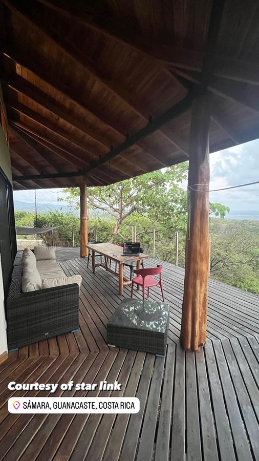 Covered wooden deck with a sofa and dining table overlooking the jungle